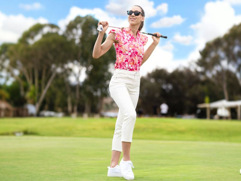 Beautiful woman wearing a red sleeveless printed golf shirt and white pants playing golf