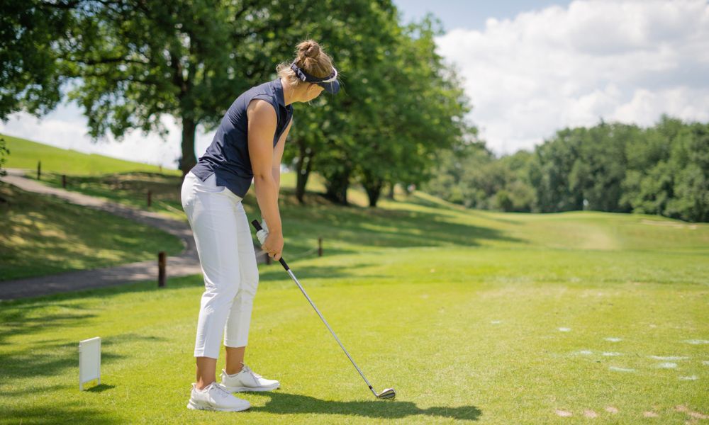Woman wearing sleeveless black golf shirt with white golf pants